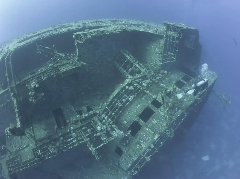 Scuba diver exploring a large sunken underwater shipwreck